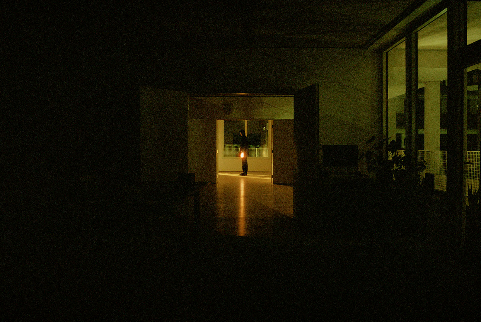 A hooded figure stands alone in a dark corridor.